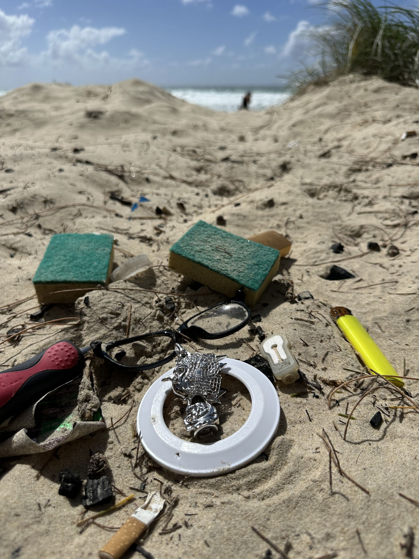 The actual silver pendant sample photographed among plastic litter found on a beach